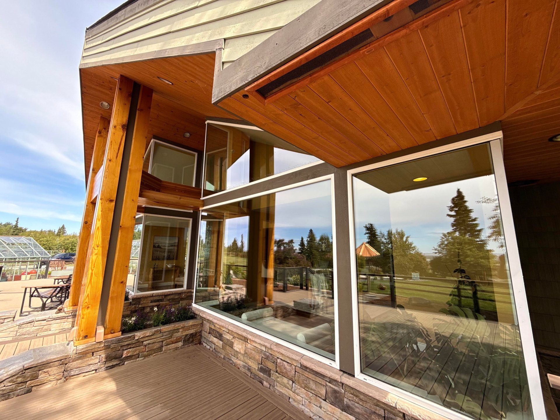 Modern covered patio with large windows and wooden beams overlooking forested landscape at sunset