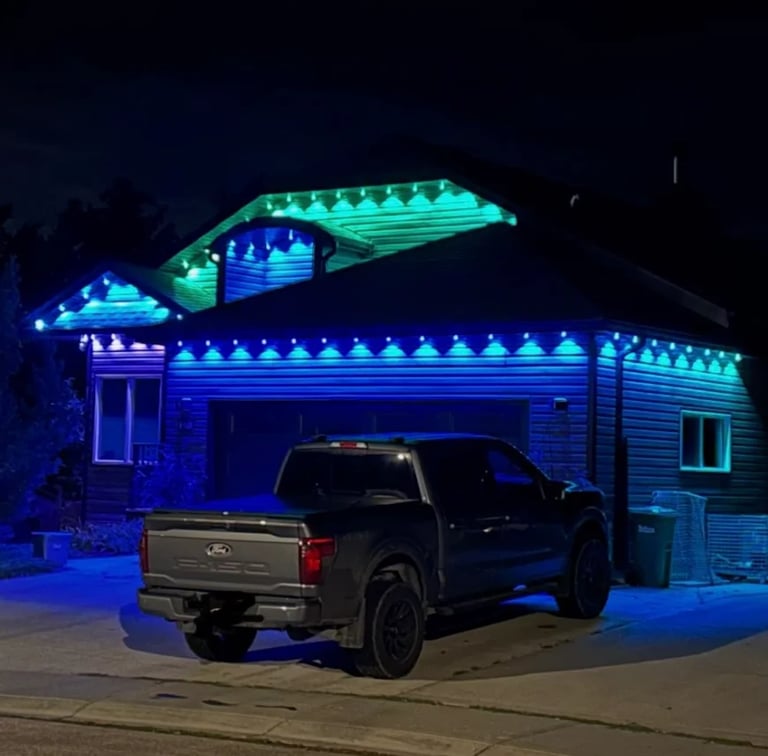 Black pickup truck parked in front of house decorated with bright blue and cyan LED lights at night